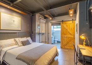 Un dormitorio con cama, mesita de noche y puerta de madera que da a un baño.