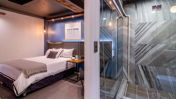 Een moderne hotelkamer met een bed, nachtkastje en een douchecabine met glazen wanden en marmeren tegels.