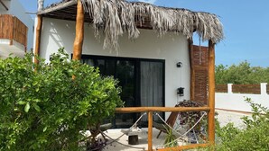 Una estructura moderna al aire libre con techo de paja, un amplio ventanal corredera y una terraza de madera.