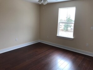 Enjoy a view of the outdoors from the large window in this room, featuring a dark hardwood floor and beige walls.