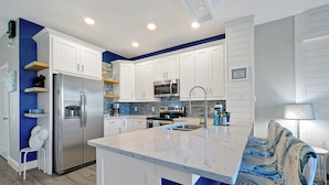 A modern kitchen with white cabinets, stainless steel appliances, and a marble countertop.