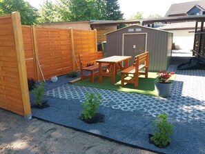 A patio with a wooden table and chairs, a small shed, and a fenced area. - Vacation apartment on the Szczecin Lagoon with garden and terrace (Ueckermünde)