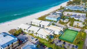 An aerial view of a coastal hotel with a beach, tennis court, and multiple buildings.