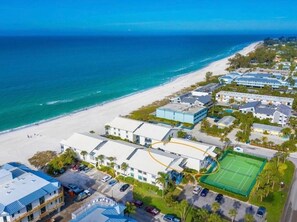 An aerial view of a coastal hotel with a beach, tennis court, and multiple buildings.