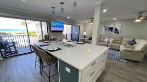 A modern kitchen with a large island, dining area with chairs, and a view of the ocean through large windows.