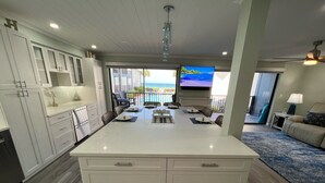A modern kitchen with a large island, white cabinetry, and a view of the ocean through a sliding glass door.