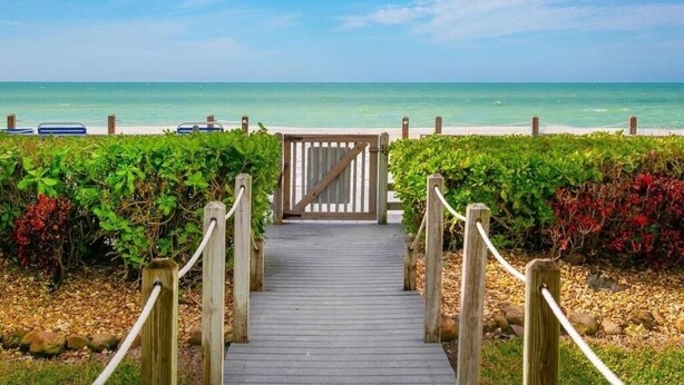 A wooden pathway leading to a beach with a gate, surrounded by greenery.
