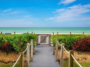 Een houten pad dat naar een strand leidt, met een poort, omringd door groen.