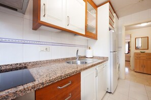 A kitchen with granite countertops, white cabinetry, a built-in dishwasher, and a refrigerator.