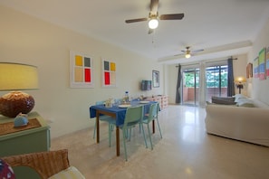 A dining area with a table set for four, a ceiling fan, and a sofa in the adjacent living room.