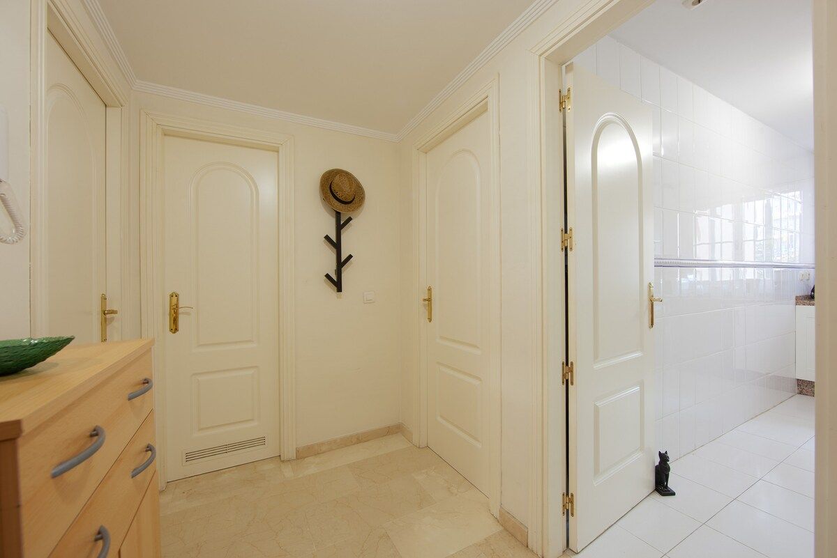 A hallway with white doors, a wooden dresser, a hat on the wall, and a cat on the floor.