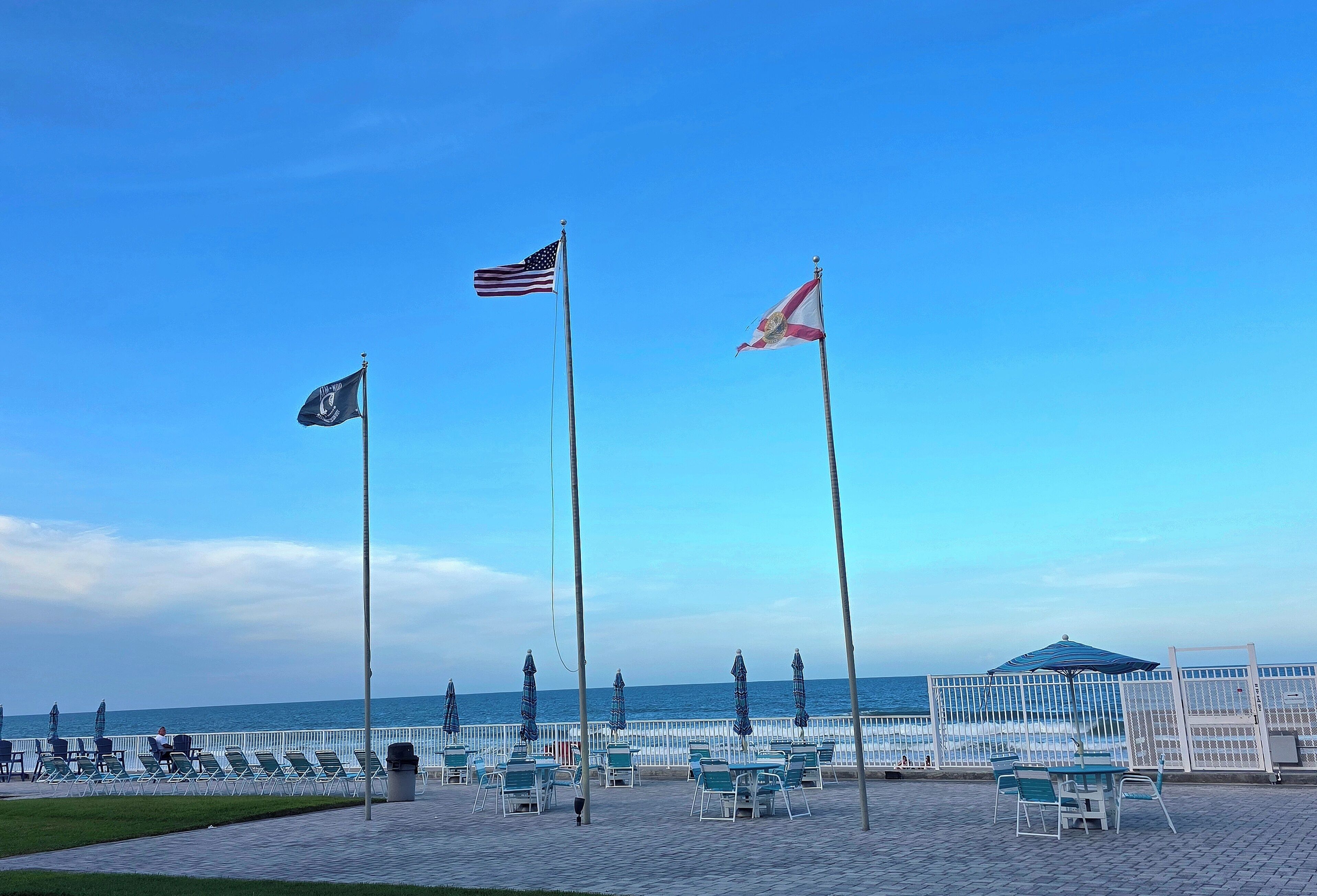 Un espace aménagé sur la plage, avec des drapeaux, des chaises, des tables et une vue sur l’océan.