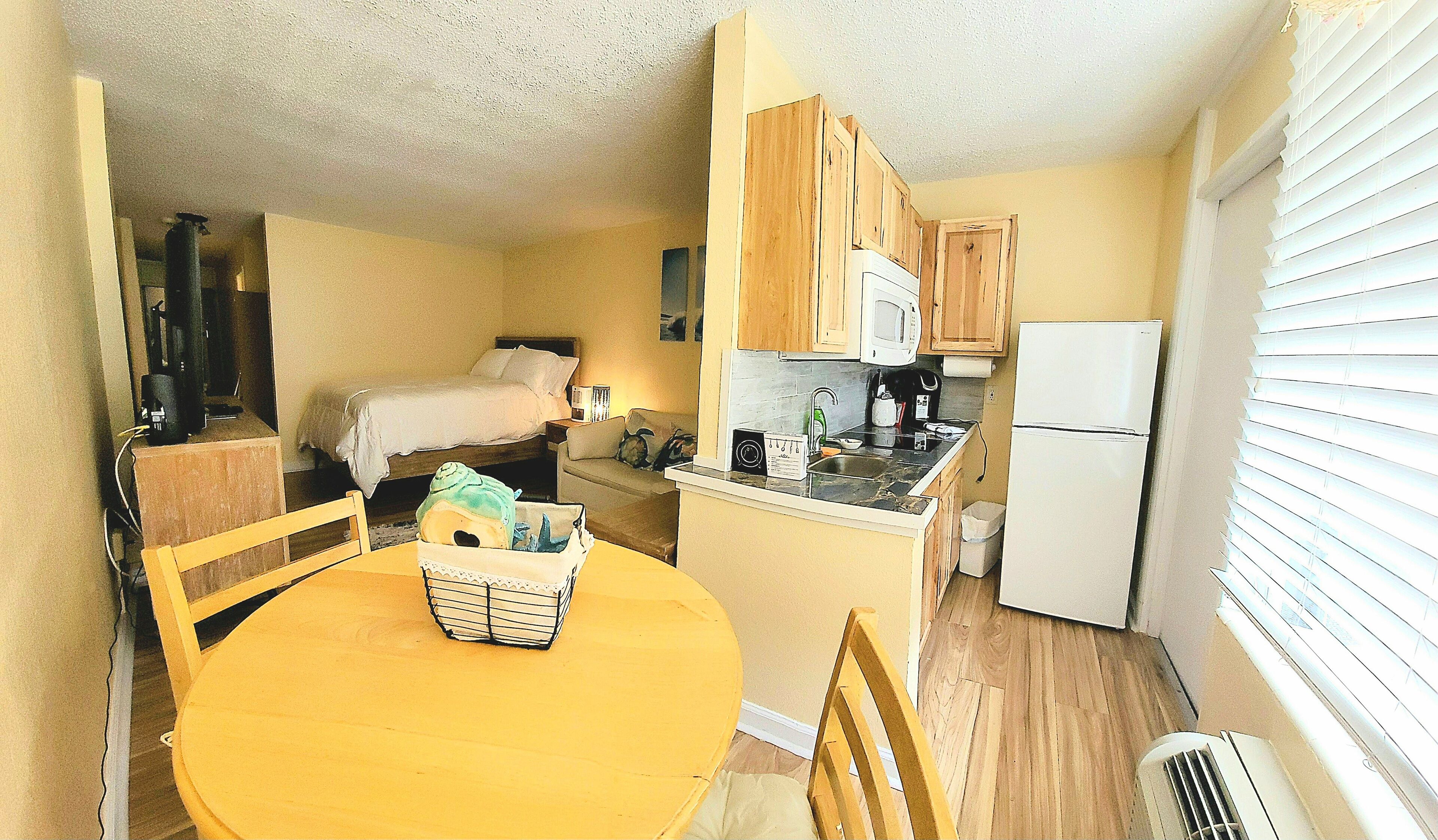 A compact kitchen with wooden cabinets, a microwave, a refrigerator, and a dining area with a yellow table and chairs.