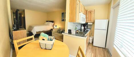 A compact kitchen with wooden cabinets, a microwave, a refrigerator, and a dining area with a yellow table and chairs.