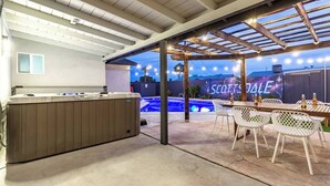 Un patio al aire libre con un jacuzzi, sillas blancas y una piscina al fondo.