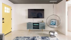 Una sala de estar moderna con una puerta amarilla, un mueble gris, una silla colgante y un cuadro grande en la pared.