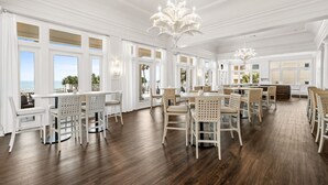 A spacious dining area with white furniture and large windows offering a view of the sea. - Beach Front Penthouse 4 Top Floor! K/K/K/K/tw/tw-Ocean Front 70 ft Balcony-Pools (Gulf Shores)