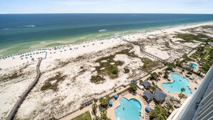 An aerial view of a beach resort with a long pier, a large swimming pool, and a sandy beach with umbrellas. - Beach Front Penthouse 4 Top Floor! K/K/K/K/tw/tw-Ocean Front 70 ft Balcony-Pools (Gulf Shores)