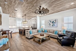 A spacious living room with a wooden coffee table, a leather sofa, and a dining area with a wooden table and chairs. - Serenity: Walk to beach, Free golf cart, Heated pool, Game room, Luxury home (Miramar Beach)