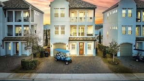 Un edificio residenziale a più piani con un ingresso garage centrale, una strada d'accesso coperta e un golf cart parcheggiato di fronte.