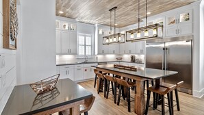 Una cucina moderna con mobili bianchi, una grande isola con sgabelli da bar, elettrodomestici in acciaio inossidabile e luci a sospensione.