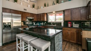 A modern kitchen with dark wooden cabinets, stainless steel appliances, and a central island with bar stools. - Spectacular Hillside Fountain HIlls home + Resort Backyard and Views! (Fountain Hills)