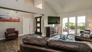 A spacious living room with a leather sofa, a television, and a view of the outdoors through large sliding glass doors. - Spectacular Hillside Fountain HIlls home + Resort Backyard and Views! (Fountain Hills)
