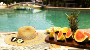 A poolside setting with a hat, sunglasses, and a fruit platter including watermelon and pineapple slices. - Hotel Rancho Leon a Place to Stay | Room 12 (Quepos)