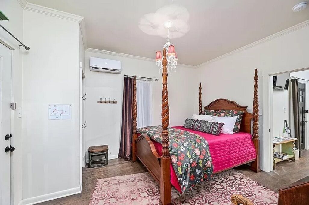 Un lit à baldaquin avec une couvre-lit à motifs floraux, un lustre et une porte blanche agrémentée d’une petite fenêtre.