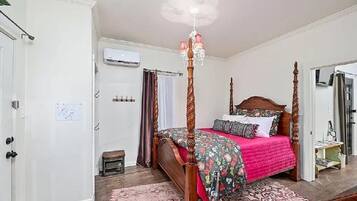 Un lit à baldaquin avec une couvre-lit à motifs floraux, un lustre et une porte blanche agrémentée d’une petite fenêtre.