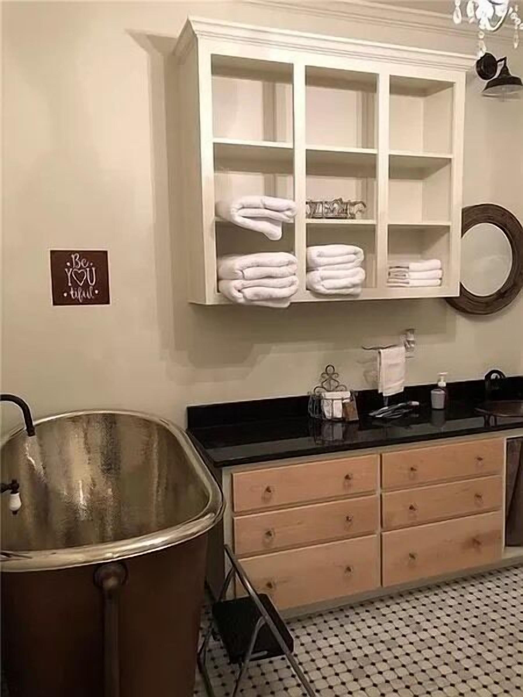 Casa de banho com uma banheira grande, um lavatório branco com gavetas, um espelho e um porta-toalhas com toalhas dobradas de forma organizada.