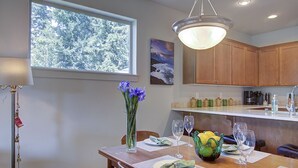 A dining area with a wooden table set for four, a vase of flowers, and a fruit bowl.