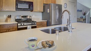 A kitchen with wooden cabinets, a stainless steel refrigerator, a microwave, a stove, and a sink.