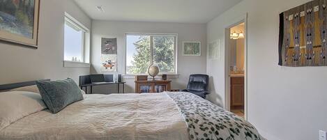 Un dormitorio con una cama grande, un escritorio con un globo terráqueo, una silla y una ventana con vistas a árboles.