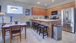 A modern kitchen with wooden cabinets, a stainless steel refrigerator, and a bar area with stools.