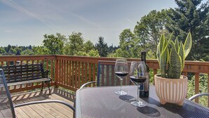 A wooden deck with a metal table, two wine glasses, a bottle, and a potted plant.