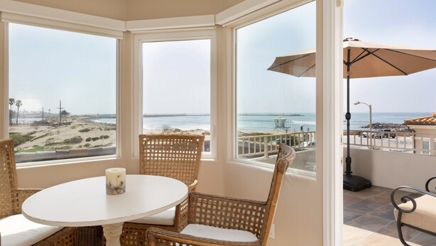 Ein Eckzimmer mit Blick auf Strand und Meer, Korbmöbel und ein Tisch mit Kerze.