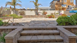 Eine Terrasse mit Steinstufen, die zu einem Sitzbereich führen, umgeben von Pflanzen und einem Pool.