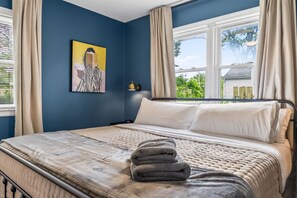 Ein Schlafzimmer mit Bett, Vorhängen an einem Fenster, einer Nachttischlampe und einem Bild an der Wand.