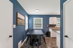 A dining area with a table and chairs, a window with blinds, a kitchen area with cabinets, and a fire extinguisher.