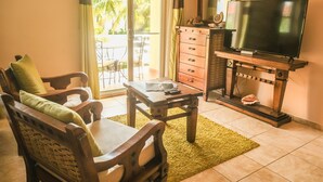 A living room with a wooden sofa, a coffee table, a TV on a wooden stand, and a sliding glass door leading to an outdoor area. - Home-like studio in Ocean Dream (Cabarete)