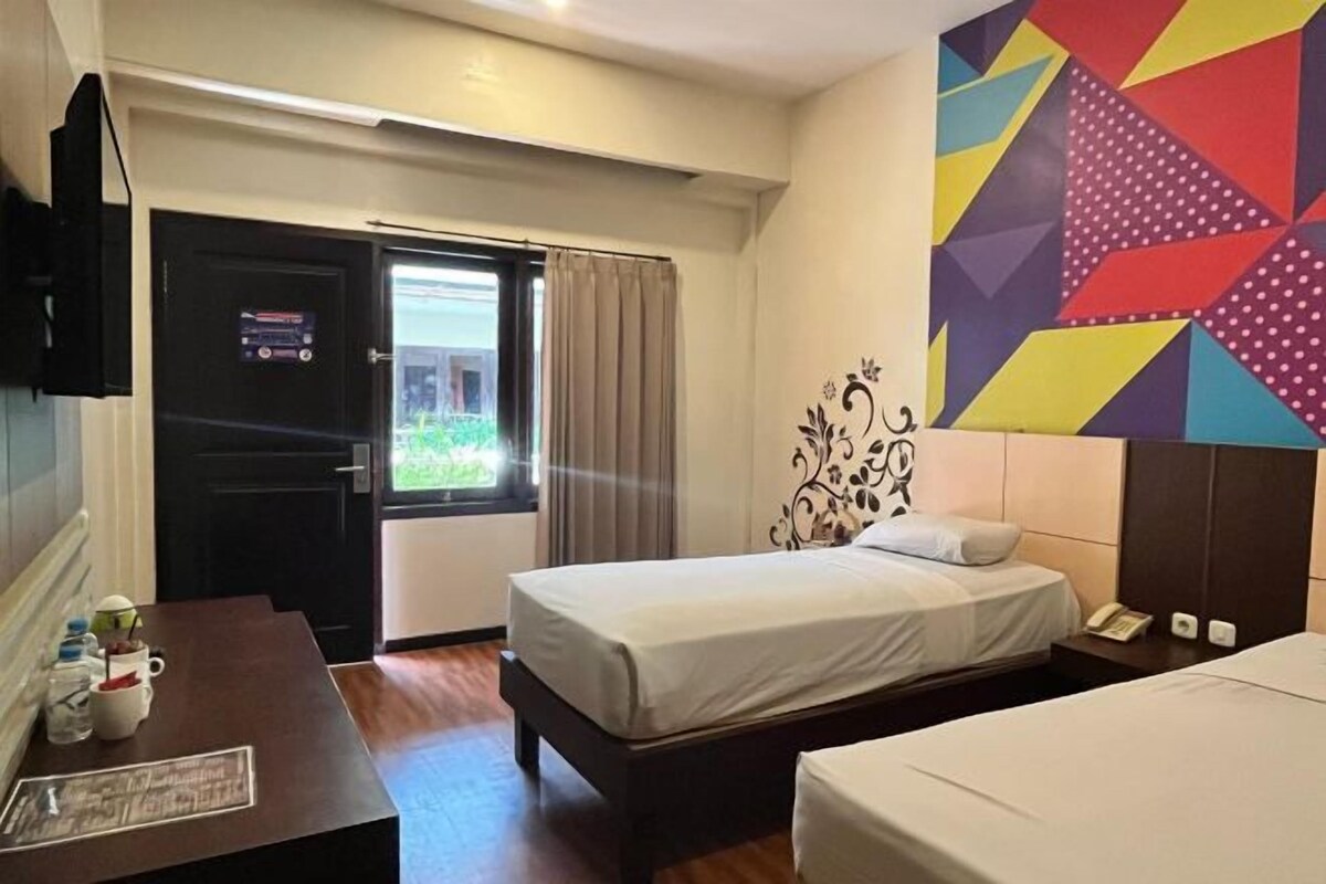 A hotel room with a bed, bedside table, and a colorful geometric wall decoration.