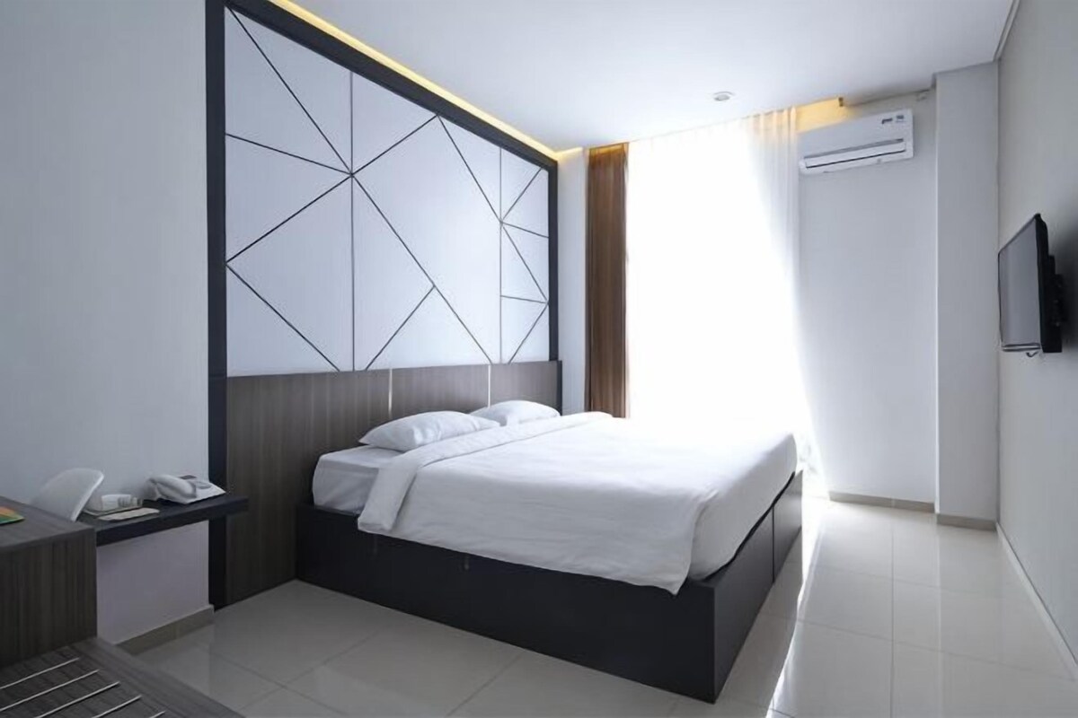 A modern hotel room with a large bed, a desk with a phone, a flat-screen TV, and a window with curtains.