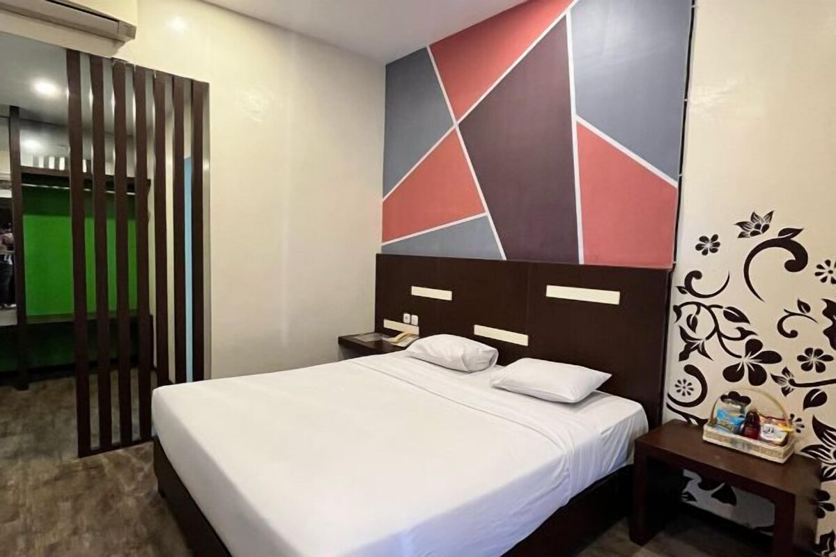 A hotel room with a bed, a nightstand, a decorative wall, and a wooden partition.