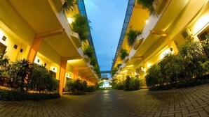 Pasillo de hotel con un camino central, flanqueado por balcones con plantas y vista al cielo al anochecer.
