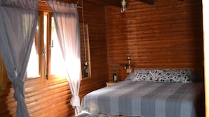 A wooden cabin bedroom with a bed, curtains, a bedside table, and a hanging light fixture. - villa chalet con piscina (Palermo)