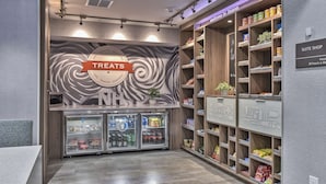 A hotel suite shop with shelves stocked with snacks and sundries, a refrigerated display case, and a sign indicating 24-hour availability. - Hampton Inn & Suites Keene (Keene)