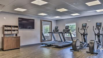 A gym with treadmills, elliptical machines, and a wooden cabinet with towels.