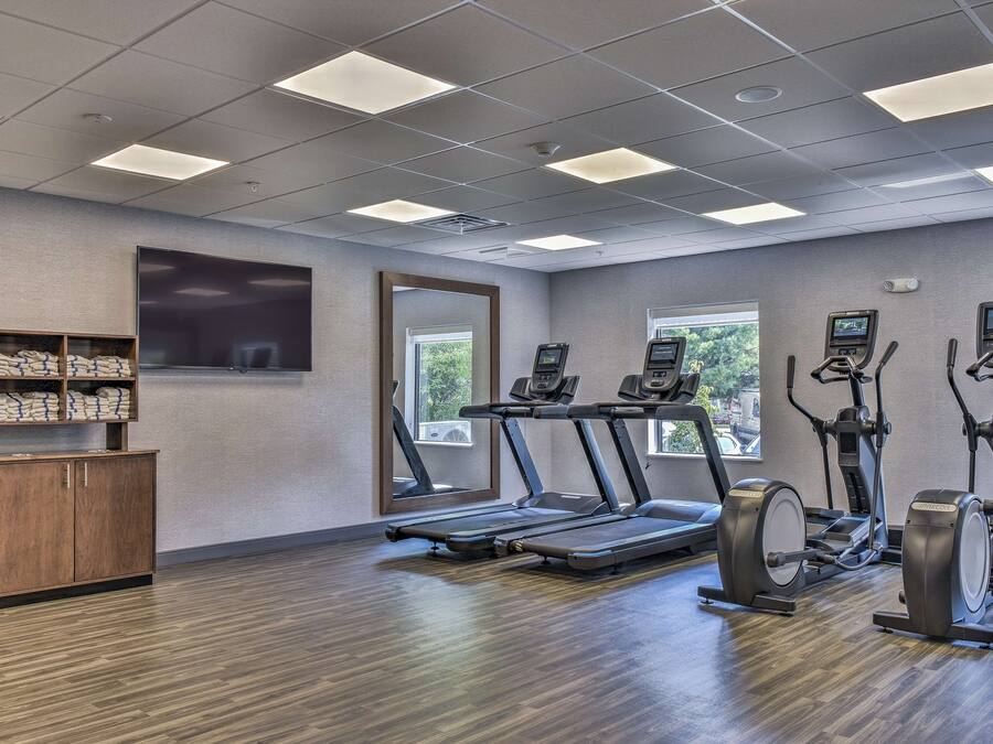 A gym with treadmills, elliptical machines, and a wooden cabinet with towels.