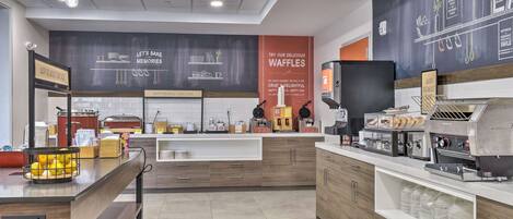 A modern kitchen area with a counter, coffee machines, and a chalkboard with menu options.